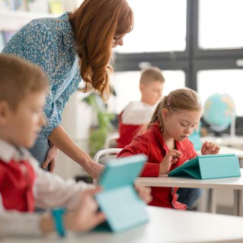 Schoolgirl with down syndrome using digital tablet during lesson in classroom at primary school.