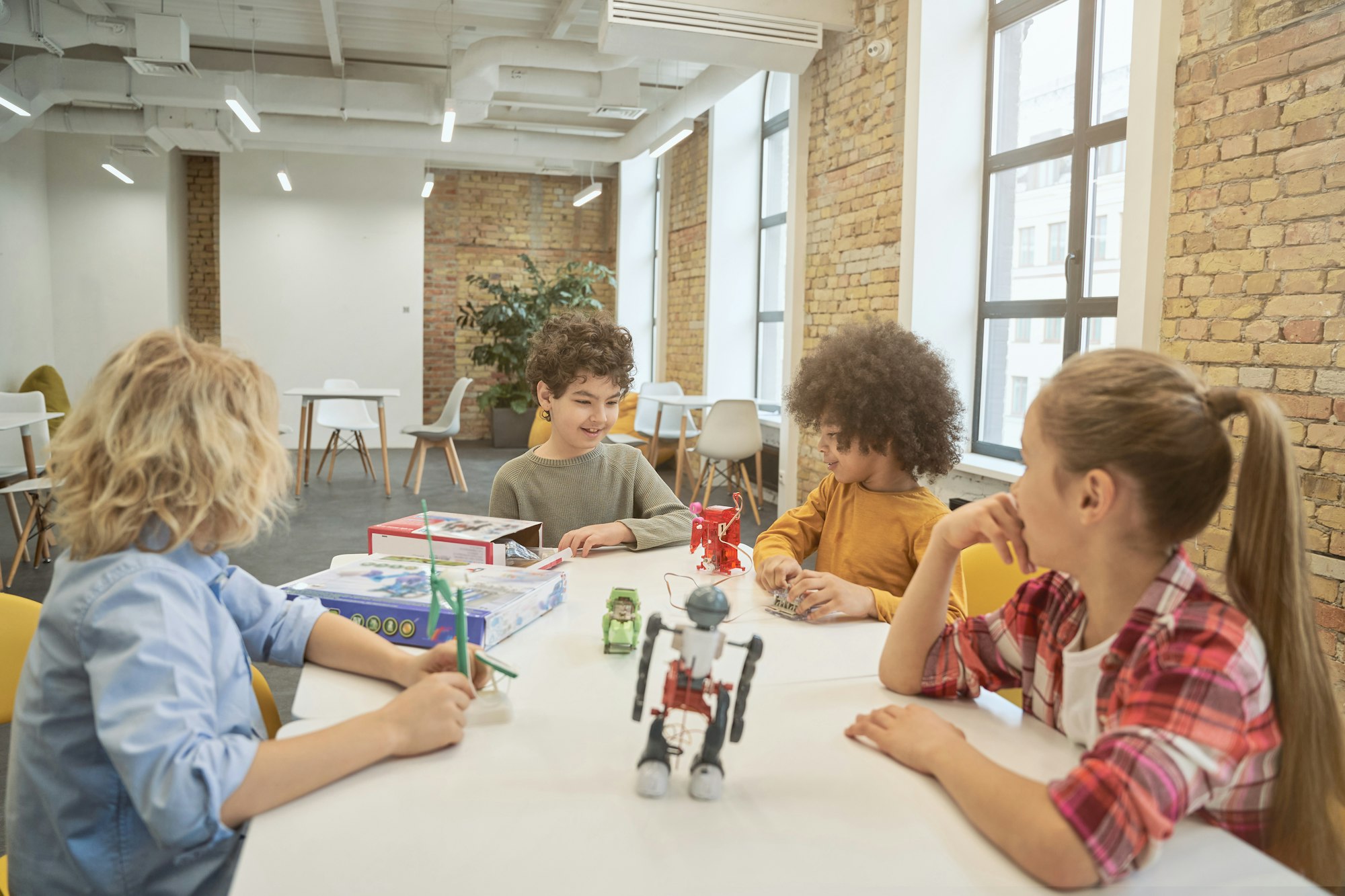 Collaboration. Clever diverse kids sitting at the table, examining technical toys full of details