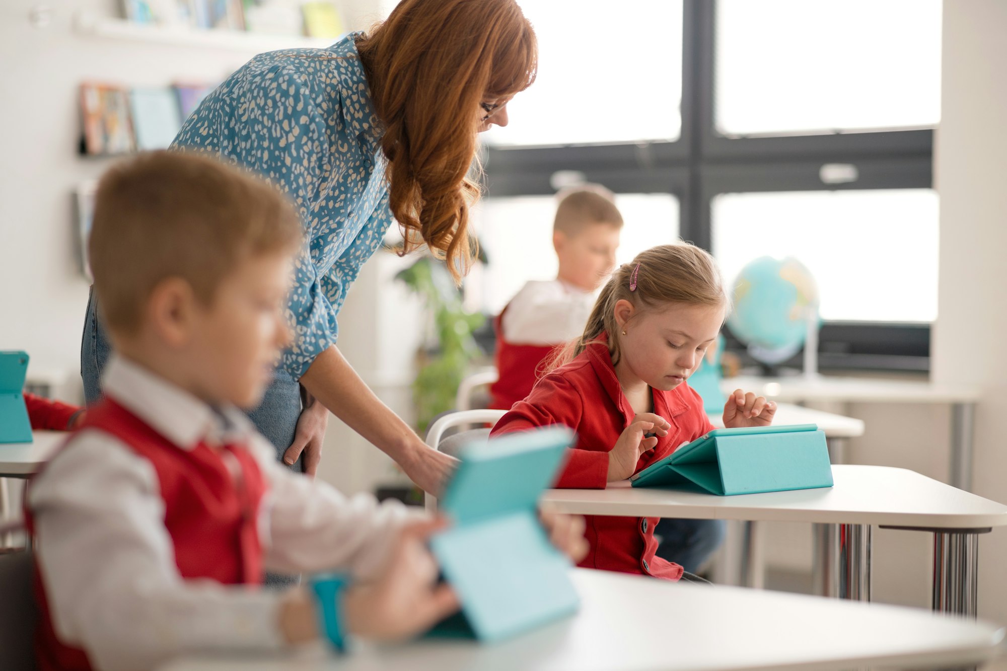 Schoolgirl with down syndrome using digital tablet during lesson in classroom at primary school.